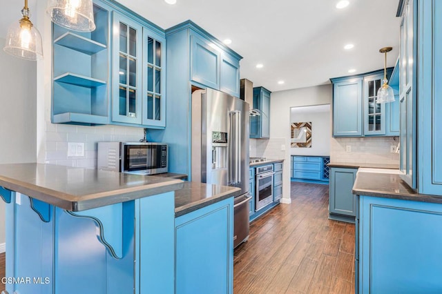 kitchen with kitchen peninsula, appliances with stainless steel finishes, blue cabinetry, a kitchen breakfast bar, and pendant lighting