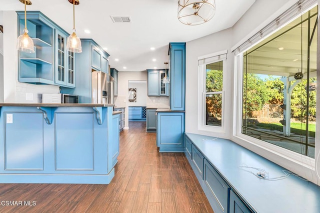 kitchen with hanging light fixtures, a kitchen bar, blue cabinets, and decorative backsplash