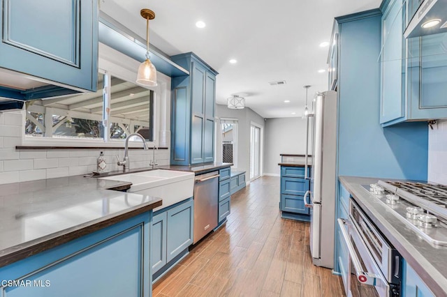 kitchen featuring light hardwood / wood-style floors, hanging light fixtures, appliances with stainless steel finishes, and blue cabinets