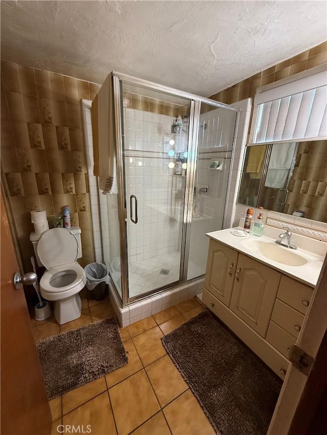 bathroom featuring tile patterned floors, a textured ceiling, a shower with door, vanity, and tile walls