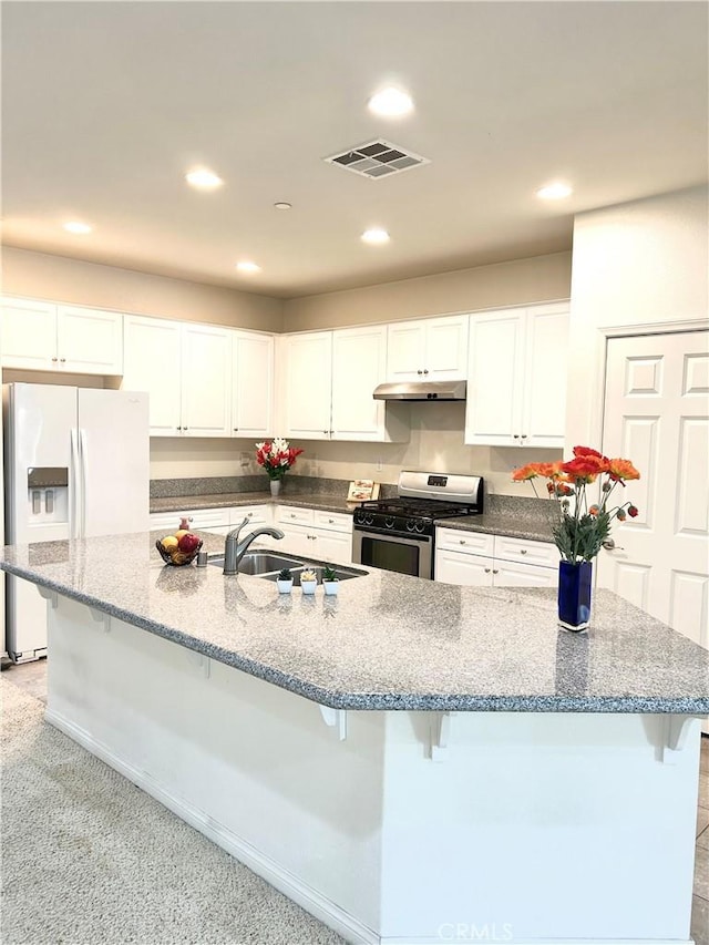 kitchen featuring sink, white fridge with ice dispenser, white cabinets, a kitchen bar, and gas range