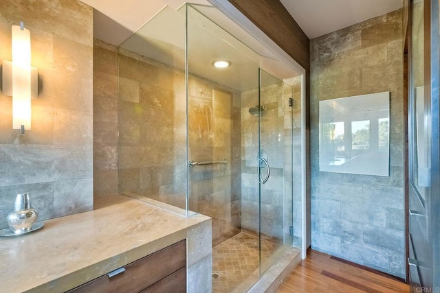 bathroom with tile walls, wood-type flooring, and a shower with door