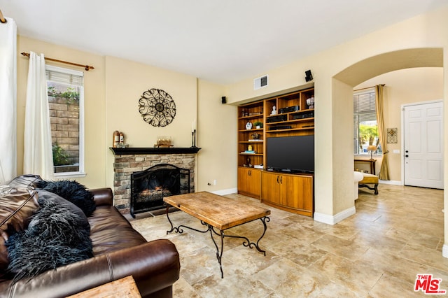 living room featuring built in shelves, a wealth of natural light, and a stone fireplace