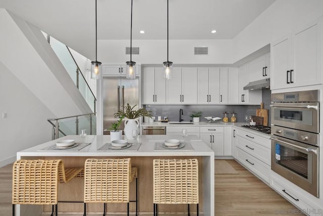 kitchen featuring a kitchen breakfast bar, hanging light fixtures, white cabinets, and an island with sink