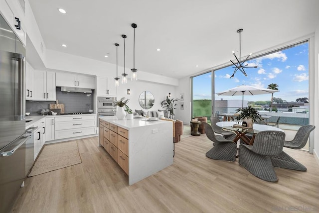 kitchen with hanging light fixtures, a kitchen island, white cabinets, and light hardwood / wood-style floors