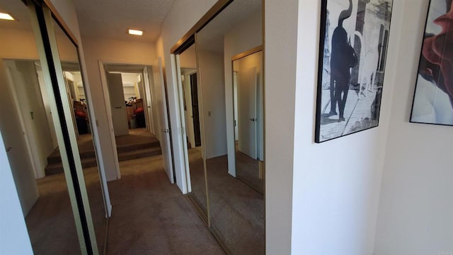 hall with a textured ceiling and dark colored carpet