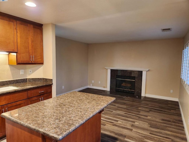 kitchen with dark hardwood / wood-style floors, a center island, sink, a tiled fireplace, and light stone counters