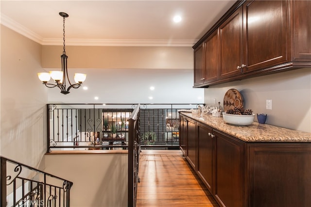 bar with an inviting chandelier, decorative light fixtures, light wood-type flooring, ornamental molding, and dark brown cabinetry