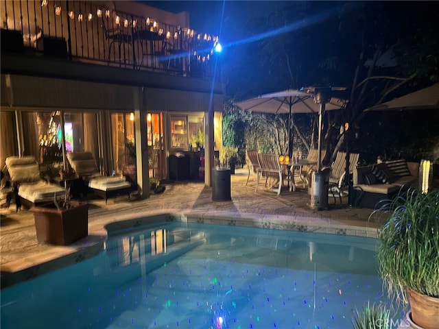 pool at night featuring a patio area