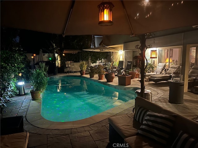 pool at night featuring an outdoor living space and a patio area