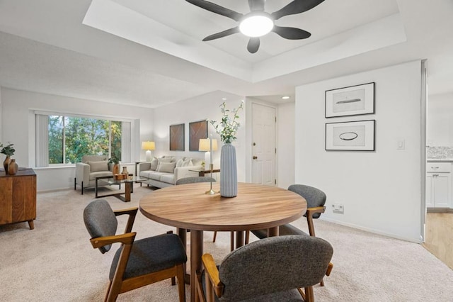 dining space featuring light carpet, ceiling fan, and a raised ceiling