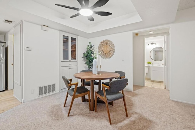 dining space featuring ceiling fan, light colored carpet, and a tray ceiling