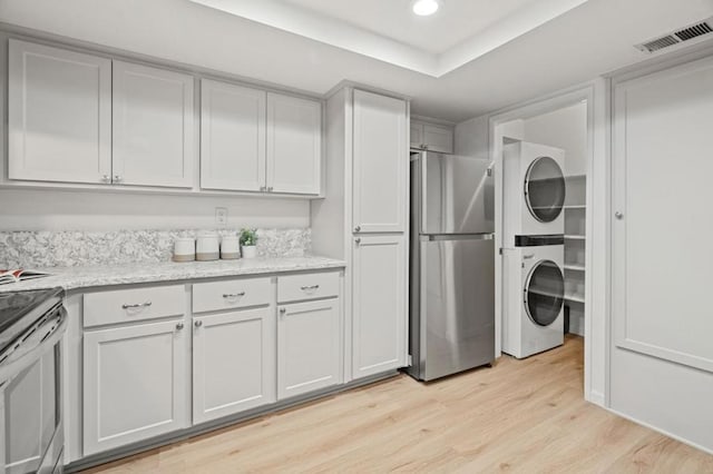 clothes washing area featuring stacked washer / dryer and light wood-type flooring