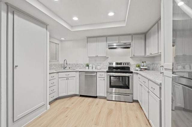 kitchen featuring appliances with stainless steel finishes, white cabinetry, light hardwood / wood-style floors, sink, and a raised ceiling