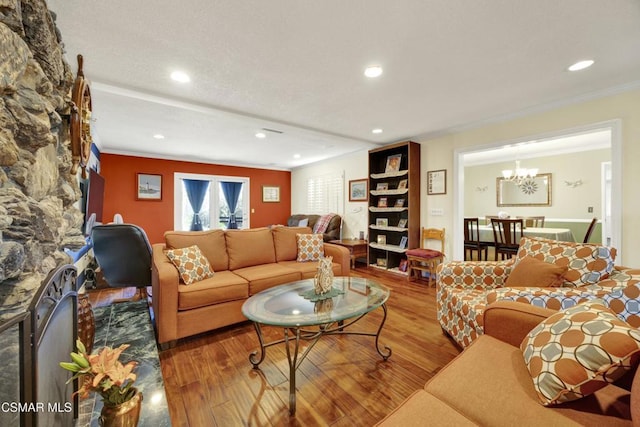 living room with wood-type flooring, a notable chandelier, a stone fireplace, and ornamental molding