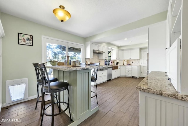 kitchen featuring tasteful backsplash, dishwasher, light stone countertops, white cabinets, and a breakfast bar