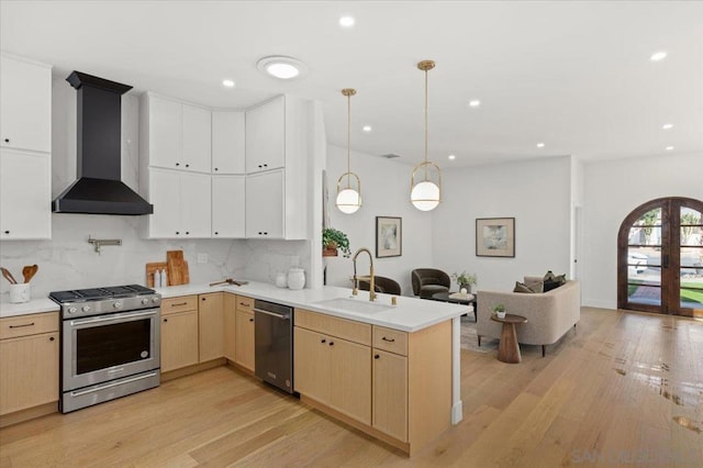 kitchen featuring decorative light fixtures, tasteful backsplash, wall chimney range hood, sink, and appliances with stainless steel finishes