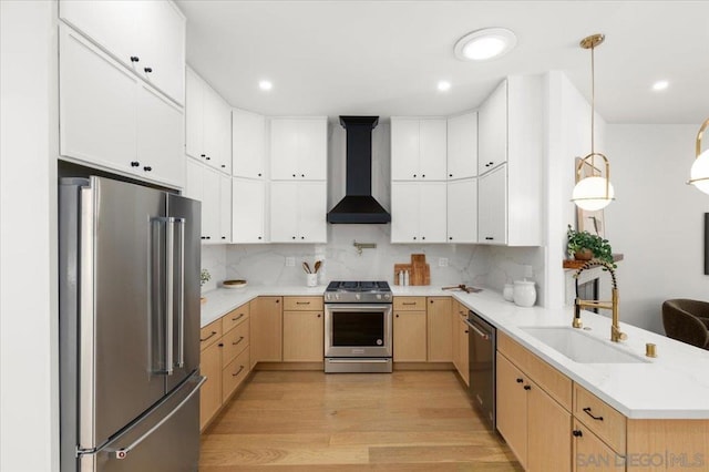 kitchen featuring stainless steel appliances, white cabinetry, decorative light fixtures, and wall chimney range hood