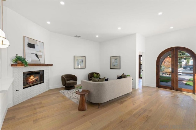 living room with light hardwood / wood-style floors, a tile fireplace, and french doors