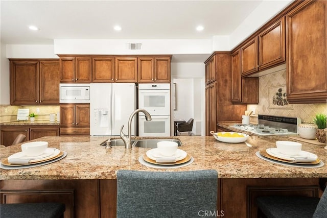 kitchen featuring sink, white appliances, backsplash, a kitchen breakfast bar, and light stone countertops