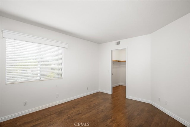 unfurnished bedroom featuring a closet, a walk in closet, and dark hardwood / wood-style floors