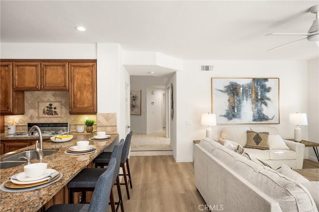 kitchen with stone counters, sink, backsplash, a kitchen breakfast bar, and light hardwood / wood-style flooring