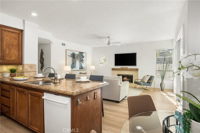 kitchen with sink, light hardwood / wood-style flooring, ceiling fan, a fireplace, and backsplash