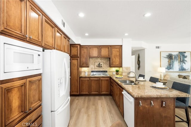 kitchen featuring a kitchen bar, sink, tasteful backsplash, kitchen peninsula, and white appliances