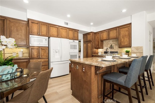 kitchen featuring white appliances, light stone counters, light hardwood / wood-style floors, a kitchen bar, and kitchen peninsula