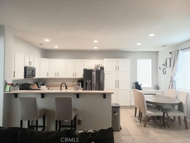 kitchen featuring a breakfast bar area, electric range, stainless steel fridge with ice dispenser, and white cabinetry