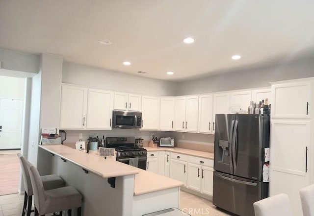 kitchen with a kitchen breakfast bar, appliances with stainless steel finishes, white cabinets, and kitchen peninsula