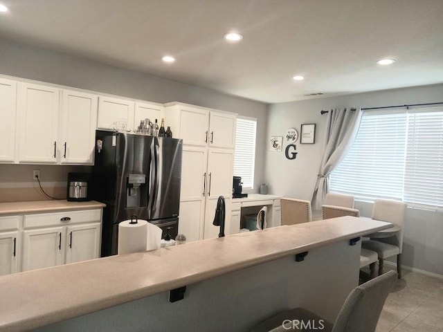 kitchen with stainless steel fridge with ice dispenser, light tile patterned floors, and white cabinetry