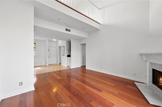 unfurnished living room with a high end fireplace, a towering ceiling, and hardwood / wood-style flooring