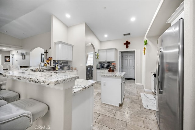 kitchen with white cabinetry, a center island, tasteful backsplash, stainless steel refrigerator with ice dispenser, and a kitchen bar