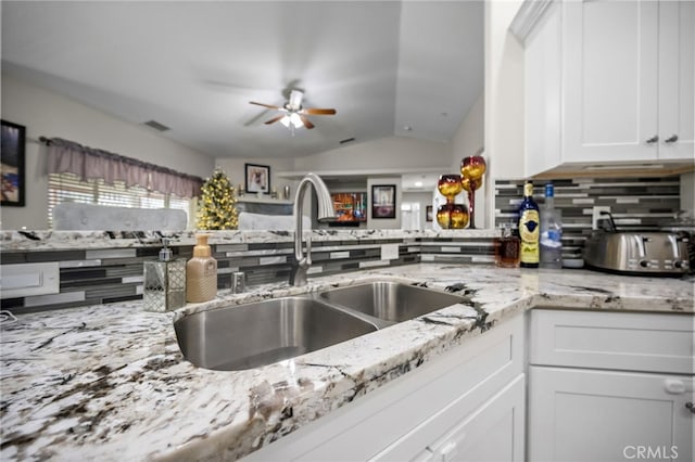 kitchen featuring decorative backsplash, light stone counters, vaulted ceiling, sink, and white cabinetry