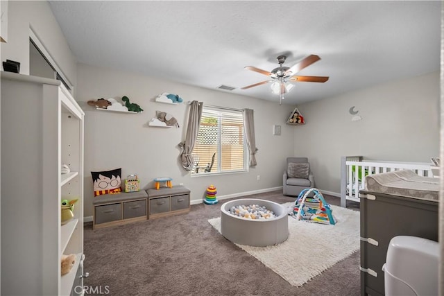 bedroom with a crib, dark carpet, and ceiling fan