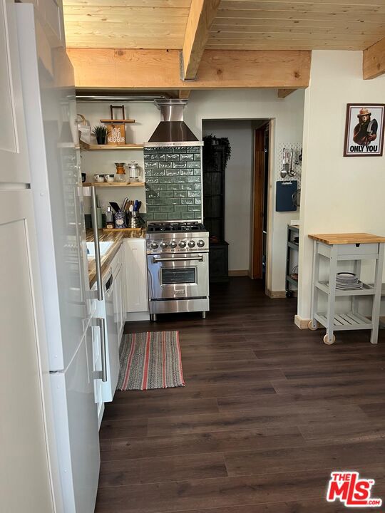 kitchen with wooden ceiling, white appliances, wall chimney range hood, and beamed ceiling