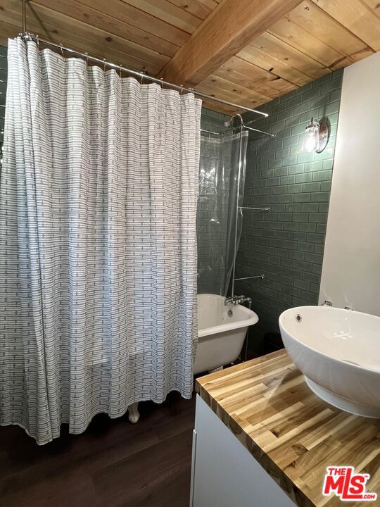 bathroom featuring beam ceiling, hardwood / wood-style floors, shower / bath combination with curtain, and wooden ceiling