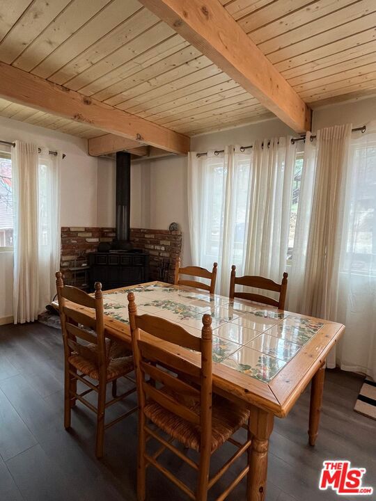 dining room featuring dark hardwood / wood-style flooring, a healthy amount of sunlight, a wood stove, and beamed ceiling