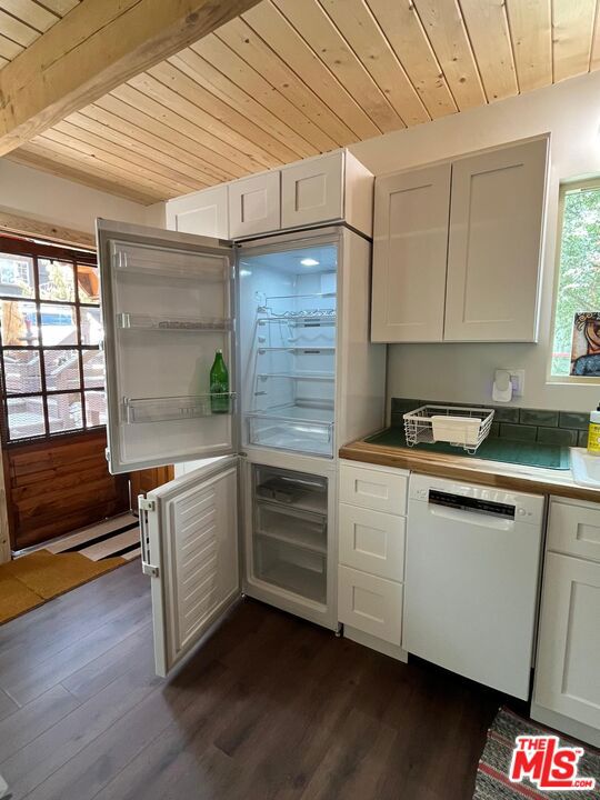 kitchen with dark hardwood / wood-style floors, beam ceiling, white dishwasher, white cabinetry, and wood ceiling