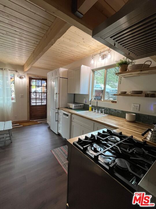 kitchen with sink, white cabinets, exhaust hood, and beamed ceiling