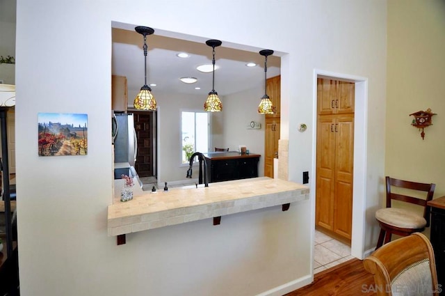 kitchen with decorative light fixtures, a breakfast bar, kitchen peninsula, light tile patterned flooring, and stainless steel fridge