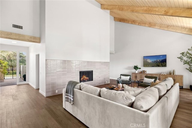 living room featuring dark wood-type flooring, wooden ceiling, a tile fireplace, and beam ceiling