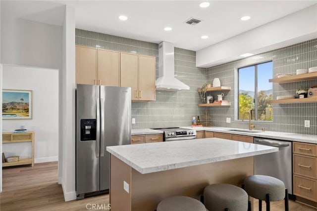 kitchen featuring appliances with stainless steel finishes, wall chimney exhaust hood, decorative backsplash, sink, and a breakfast bar area