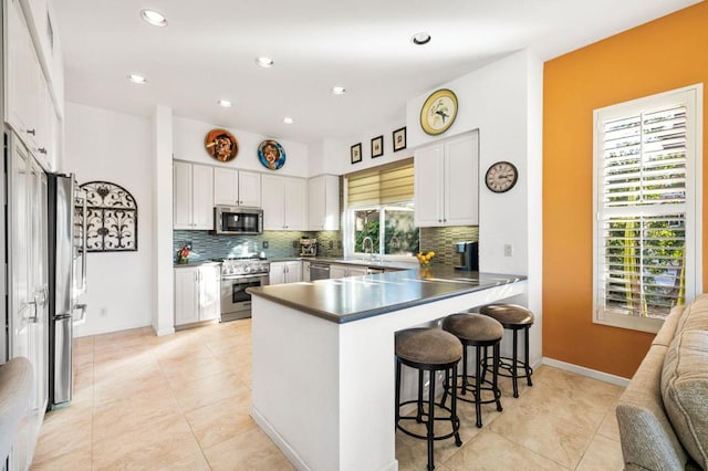 kitchen with white cabinetry, kitchen peninsula, tasteful backsplash, a kitchen breakfast bar, and high quality appliances