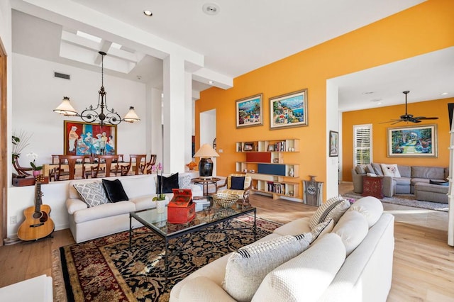 living room with light wood-type flooring, ceiling fan with notable chandelier, and beamed ceiling