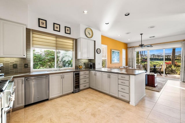 kitchen with kitchen peninsula, appliances with stainless steel finishes, tasteful backsplash, wine cooler, and white cabinets