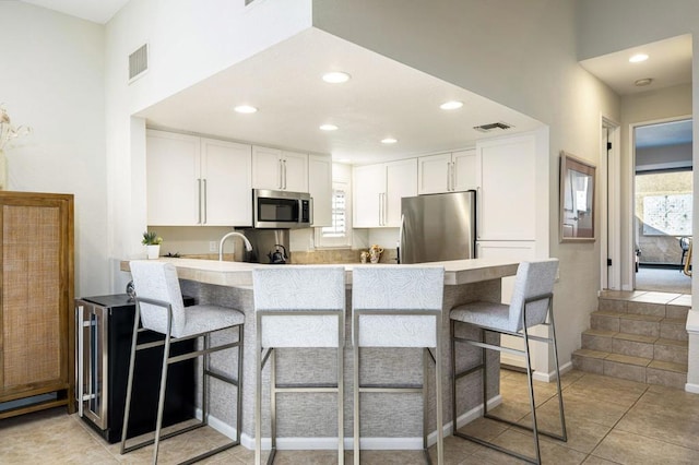 kitchen with kitchen peninsula, a kitchen bar, appliances with stainless steel finishes, and white cabinetry