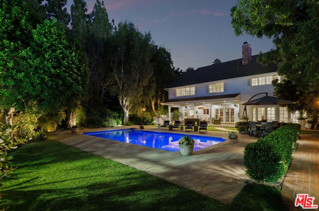 pool at dusk featuring a patio area, outdoor lounge area, french doors, and a lawn