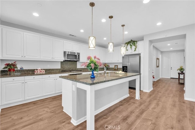 kitchen featuring stainless steel appliances, white cabinets, dark stone counters, and an island with sink